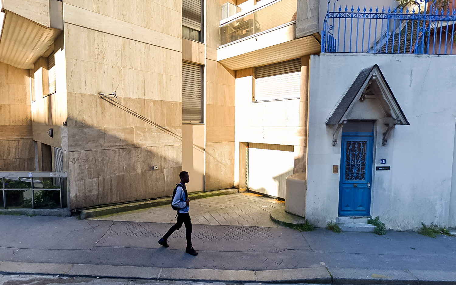 Un étudiant en train sur le trottoir. Derrière lui, l'image est comme coupée en deux avec à gauche les couleurs chaudes du coucher de soleil et à droite les couleurs froides d'un bâtiment